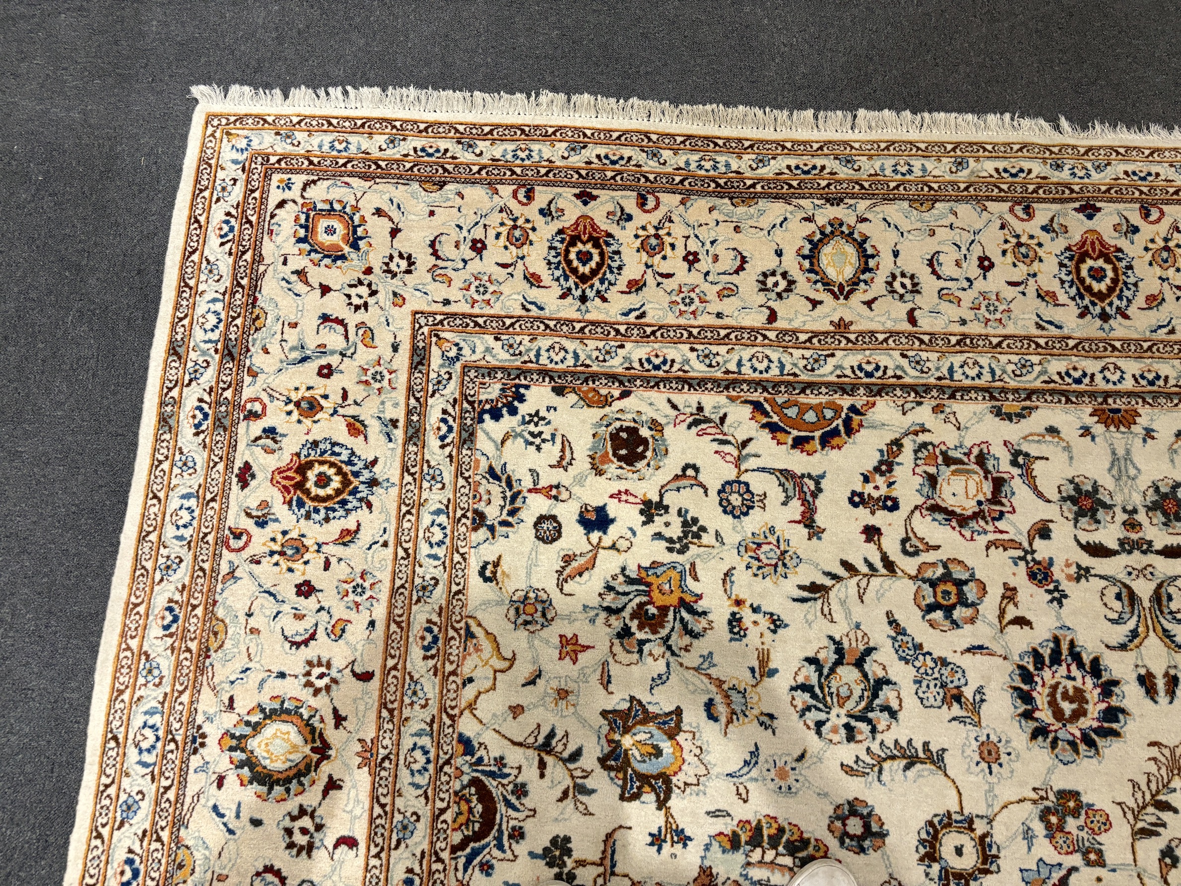 A Kashan ivory ground carpet, central field of foliate motifs, multi bordered, 400 x 308cm, Please note this lot attracts an additional import tax of 5% on the hammer price